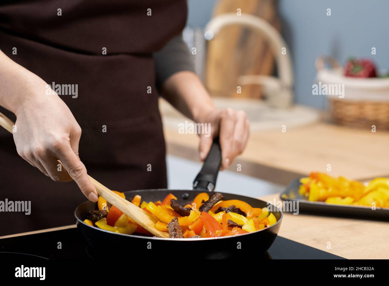 Hände einer jungen Frau, die Gemüseeintopf mit Holzlöffel mischt, während sie die Bratpfanne am Griff hält Stockfoto