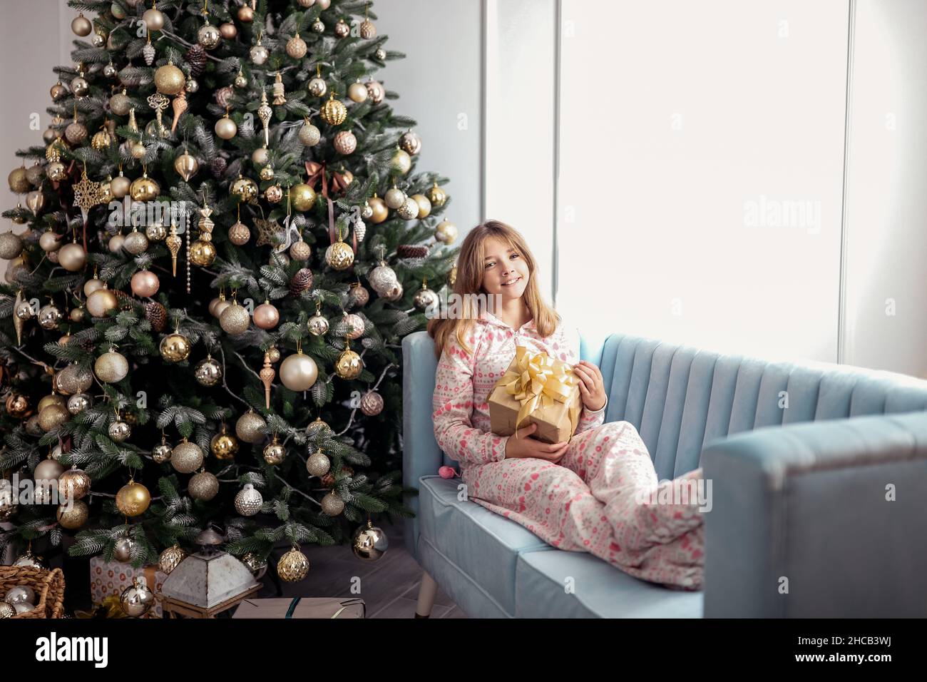 Teenager-Mädchen mit einem Geschenk in der Nähe eines Neujahrsbaums oder in einem weihnachtlichen Interieur. Stockfoto