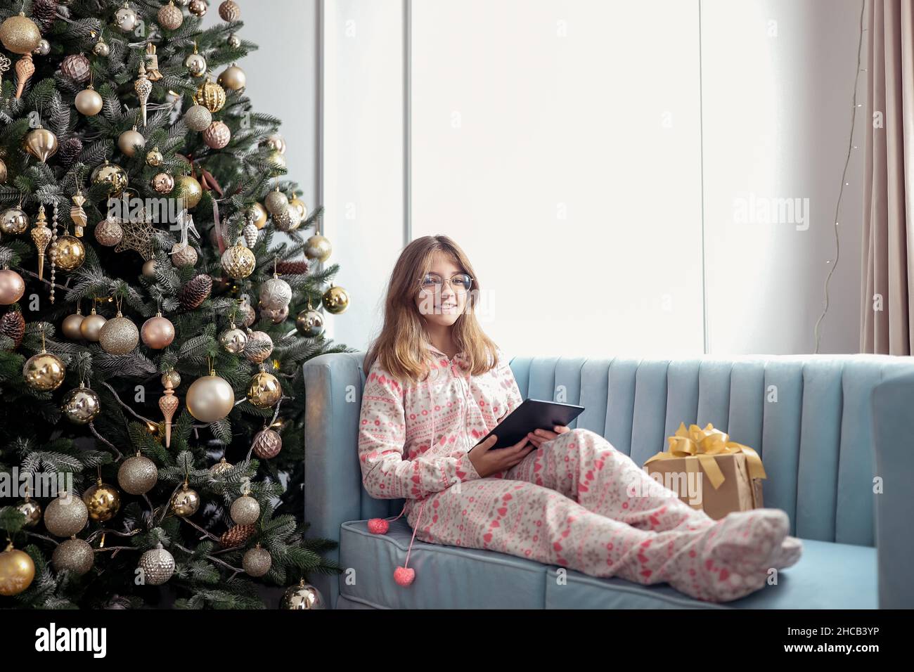 Teenager-Mädchen mit einem Tablet in der Nähe eines Neujahrsbaums oder in einem weihnachtlichen Innenraum. Stockfoto
