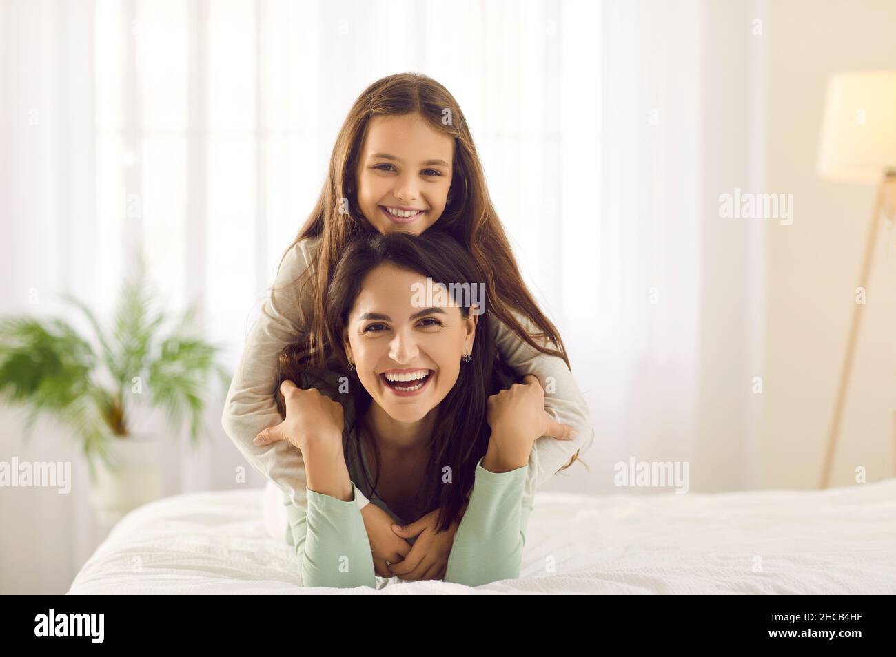 Porträt einer glücklichen jungen Mutter und einer kleinen Tochter, die zu Hause auf dem Bett kuscheln Stockfoto