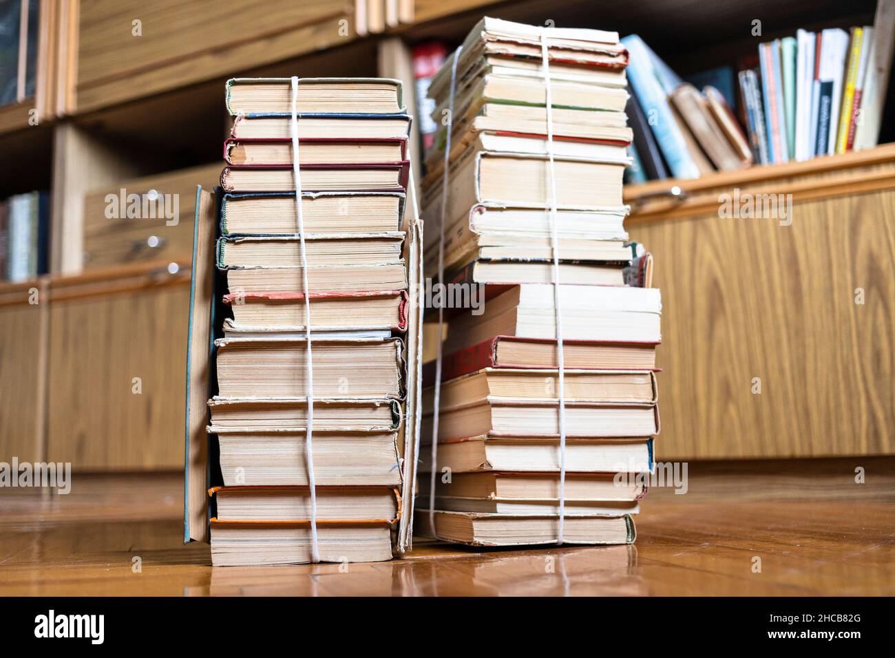 Zwei Stapel alter Bücher, mit Garn gebunden, auf Parkettboden im Wohnzimmer neben dem Bibliotheksschrank Stockfoto
