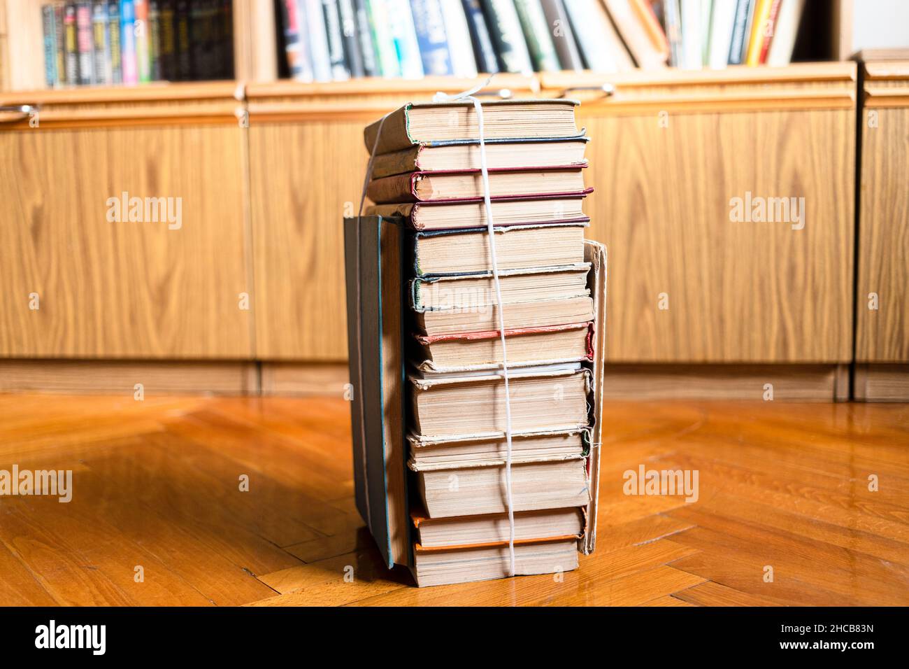 Stapel von gebrauchten Büchern mit Verpackungsfaden auf Parkettboden in der Nähe von Bibliotheksschrank im Wohnzimmer gebunden Stockfoto