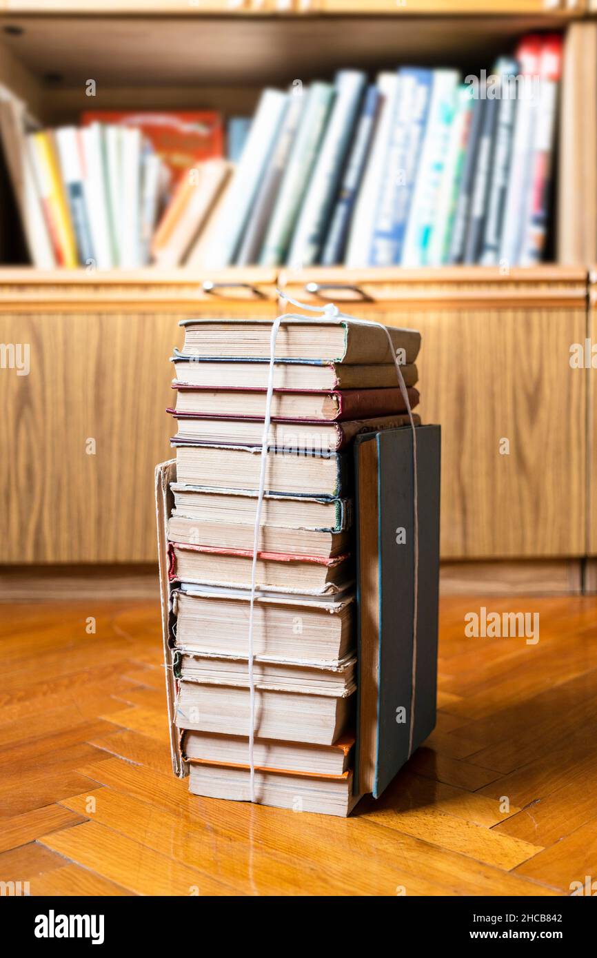 Stapel alter Bücher, die mit einem Seil auf dem Parkettboden in der Nähe des Bücherregals gebunden sind Stockfoto