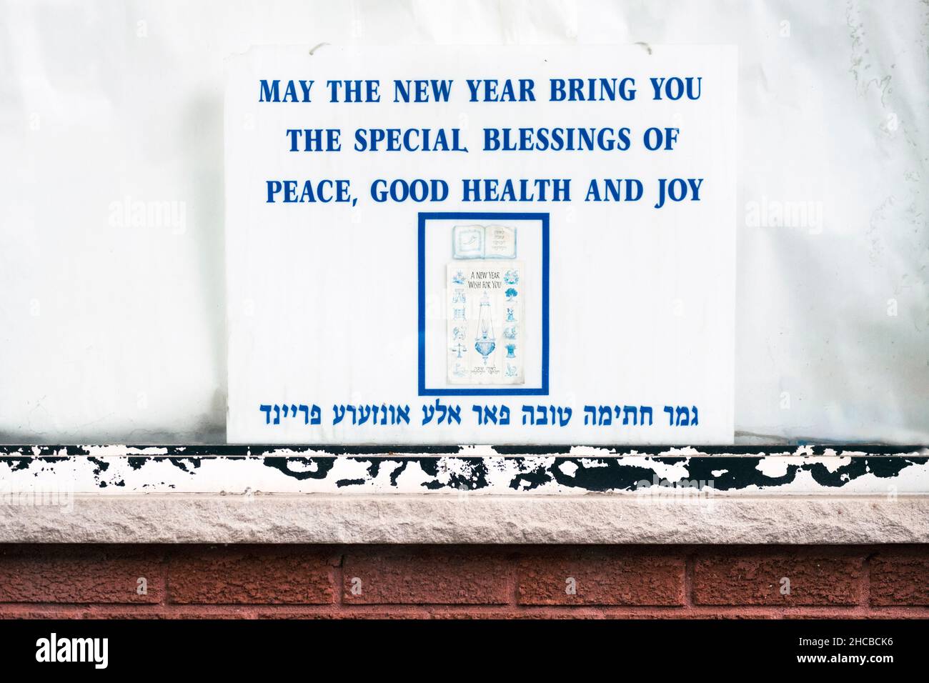 Ein jiddischer und englischer Gruß für New Years im Fenster einer Druckerei auf der Lee Avenue in Williamsburg, Brooklyn, New York City. Stockfoto