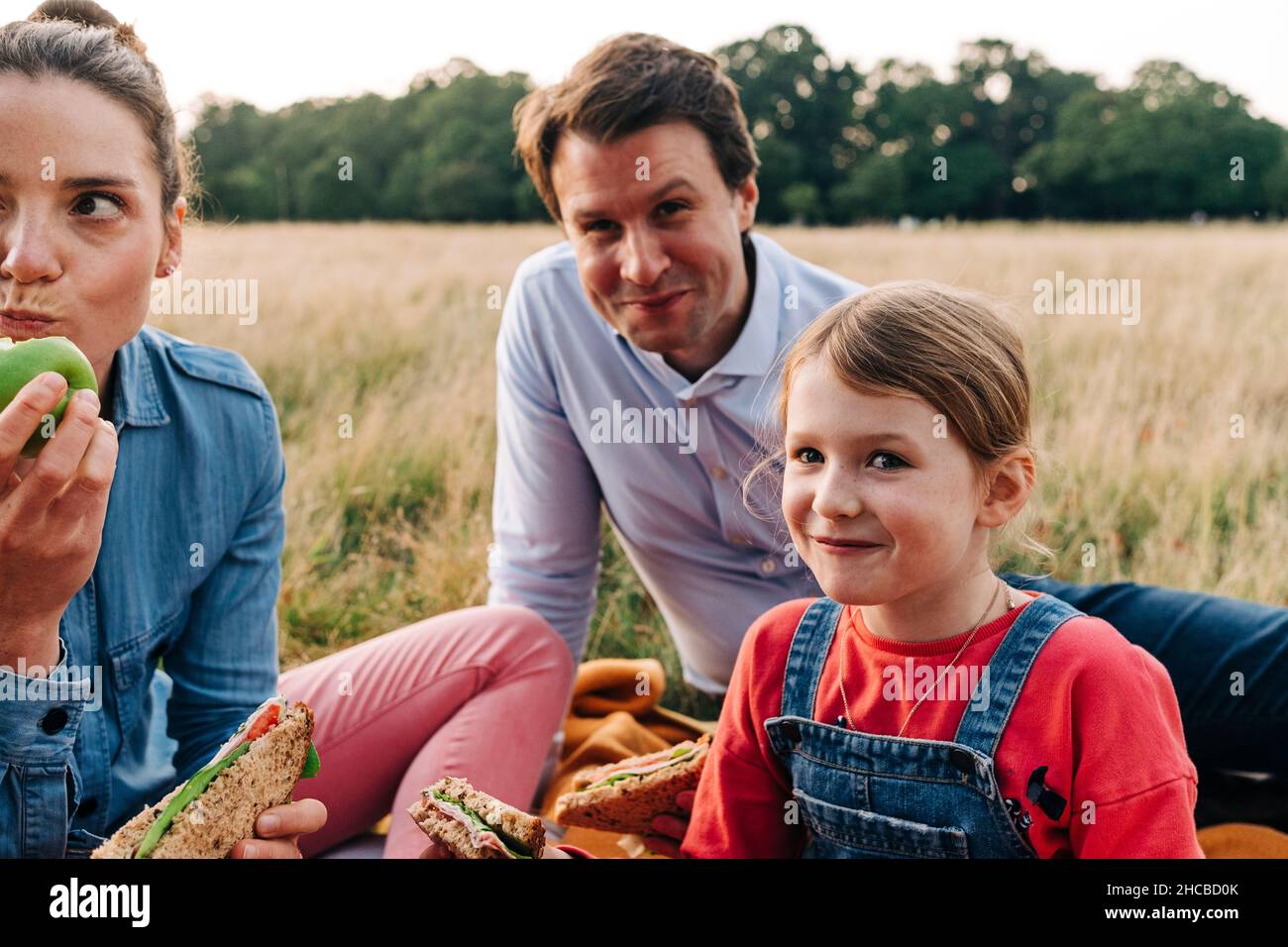 Lächelnde Tochter, die mit den Eltern im Park ein Sandwich gemacht hat Stockfoto