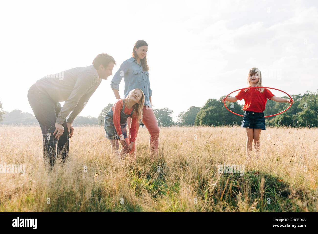 Eltern und Schwester sehen Mädchen an, die im Park mit dem Hula Hoop Reifen spielen Stockfoto