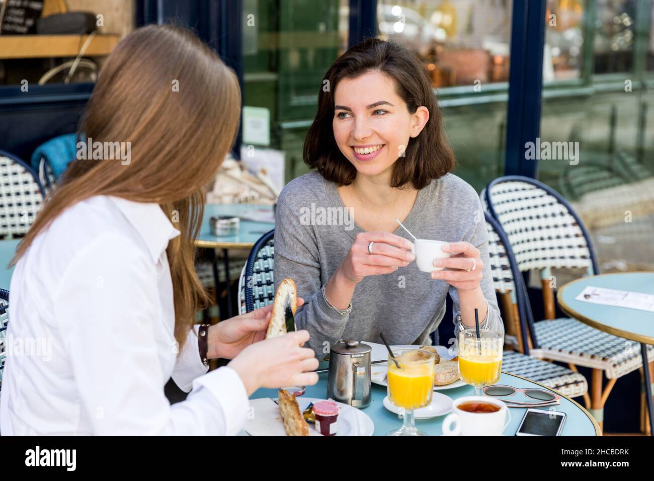 Junge Frau, die sich mit einem Freund unterhielt und im Café Baguette butterte Stockfoto