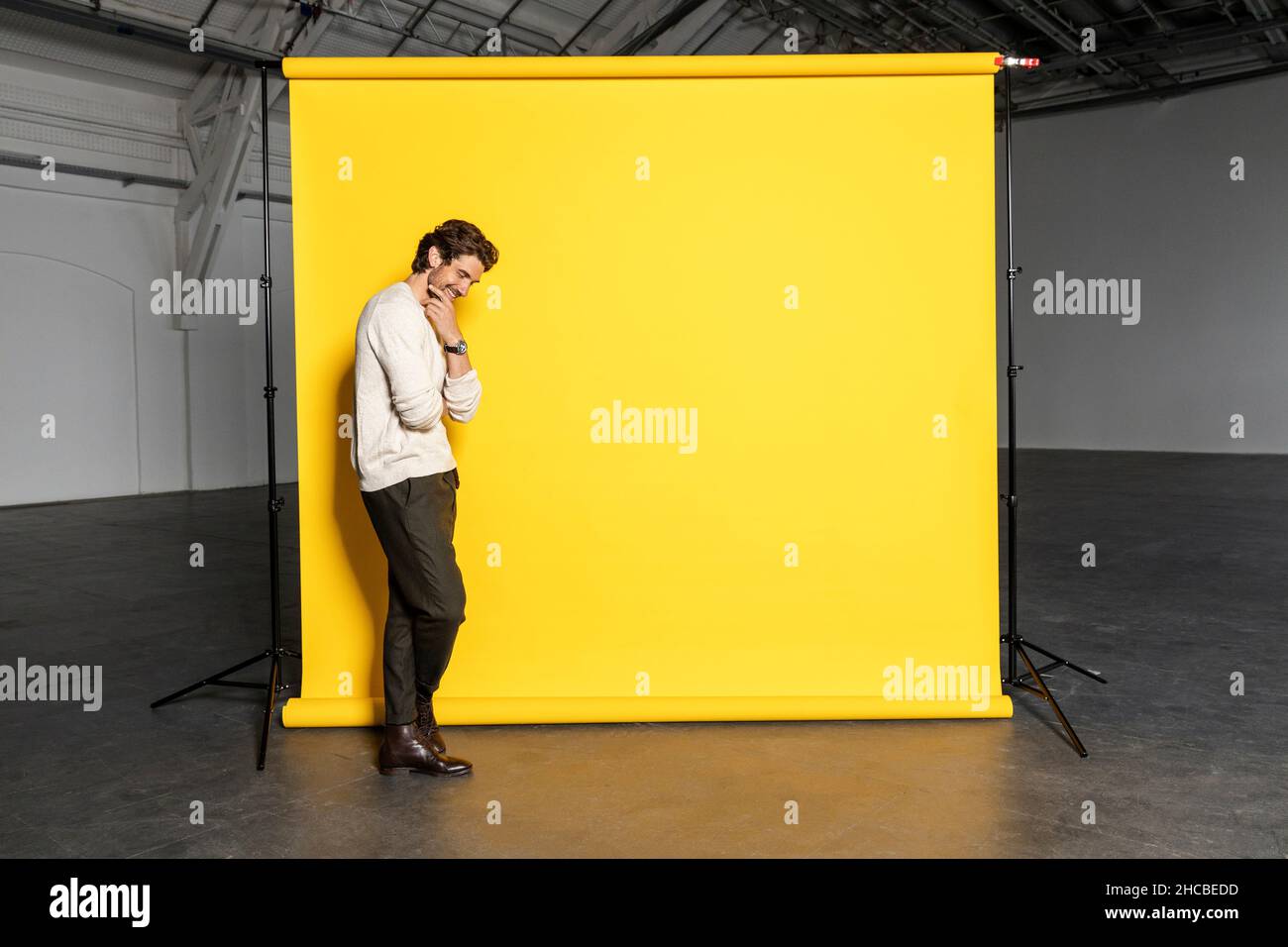 Geschäftsmann mit der Hand am Kinn vor gelbem Hintergrund in der Industriehalle Stockfoto
