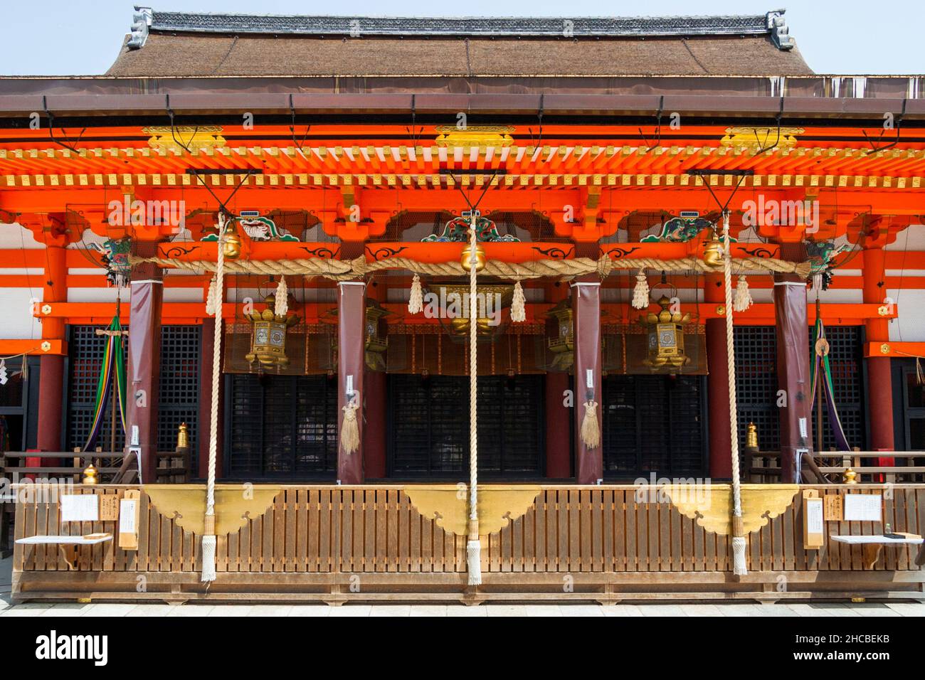 Die Haupthalle des Yasaka-Schreines in Kyoto. Orangefarbenes Holzgebäude, hängende Glockenseile und Sammelbox über die gesamte Front. Stockfoto