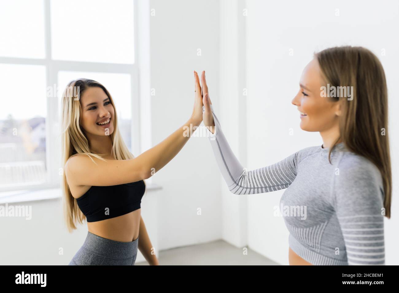 Lächelnde Fitness-Frauen heben die Hände, um eine hohe fünf während des Trainings zu geben. Fröhliche sportliche Frauen genießen das Fitnesstraining in einem Fitnessstudio. Stockfoto