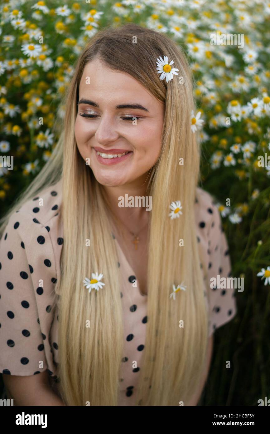 Glückliche Frau mit geschlossenen Augen trägt Blumen auf langen blonden Haaren Stockfoto