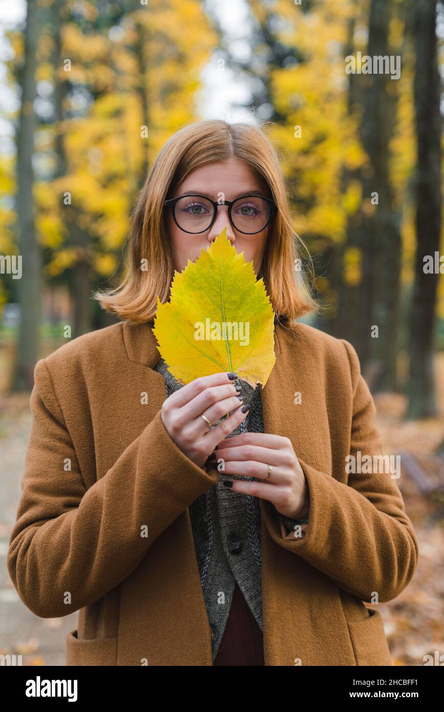 Frau hält Herbstblatt vor dem Mund im Park Stockfoto