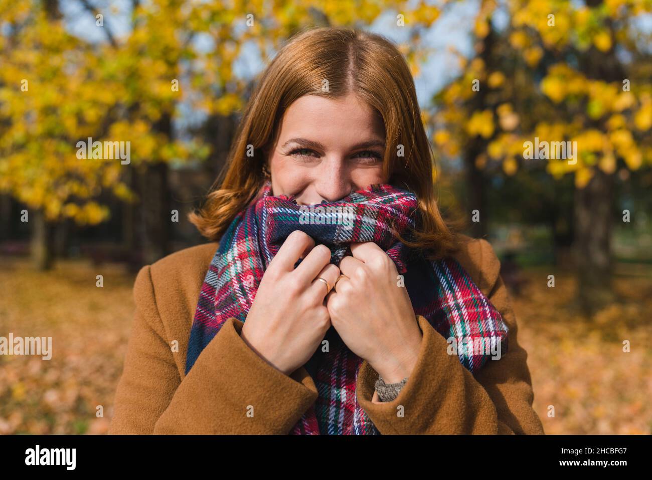 Glückliche Frau, die im Park den Mund mit Stola bedeckt Stockfoto