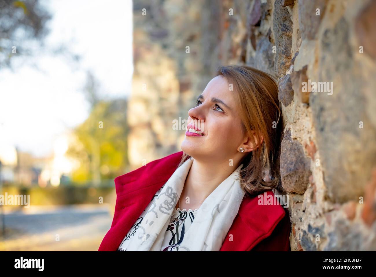 Nachdenkliche Frau, die sich an einer Steinwand lehnt Stockfoto