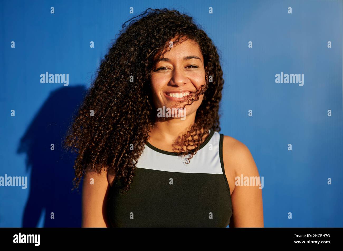 Lächelnde Sportlerin mit lockigen Haaren an sonnigen Tagen Stockfoto