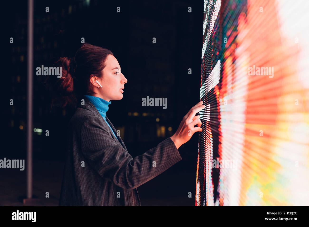 Geschäftsfrau mit Ohrhörern, die nachts über einen interaktiven Informationsstand mit Touchscreen verfügen Stockfoto
