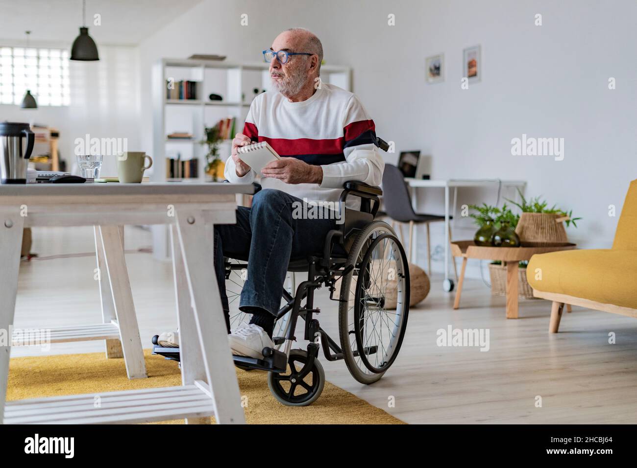 Geschäftsmann mit körperlicher Behinderung schreibt zu Hause auf Notizblock Stockfoto