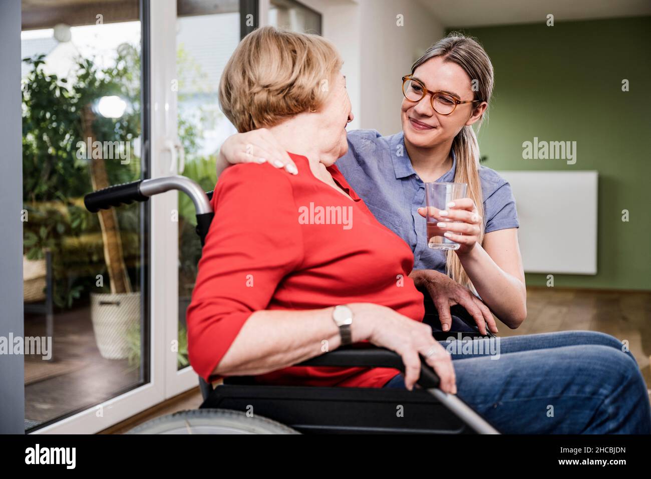 Lächelnder Pflegeassistent, der behinderten Frauen zu Hause Wasser gibt Stockfoto