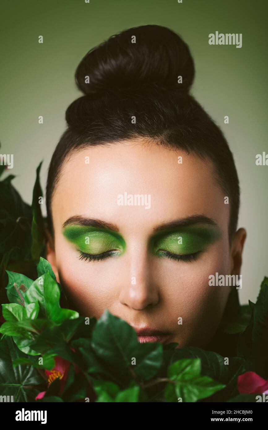 Frau mit Augen-Make-up und grünen Pflanzen vor grünem Hintergrund Stockfoto