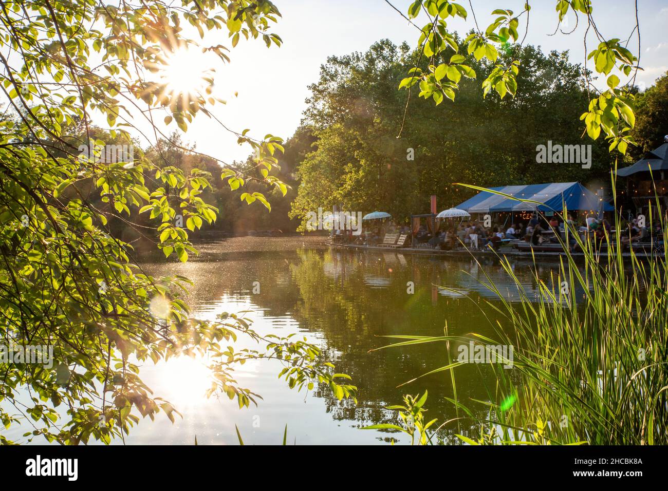 Deutschland, Bayern, München, Sonnenuntergang über dem Mollsee im Westpark mit Biergarten im Hintergrund Stockfoto