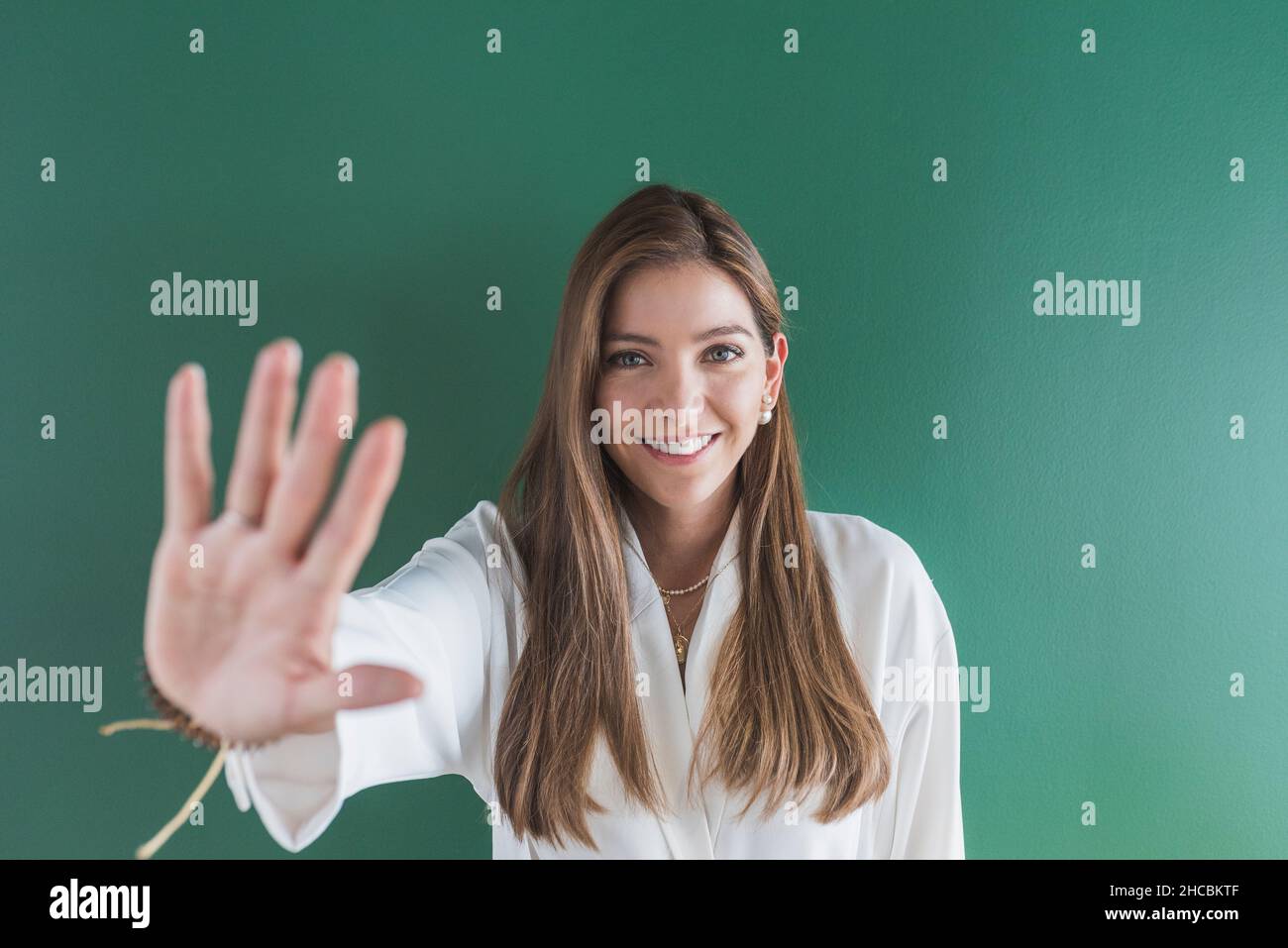 Lächelnde Frau mit Stopphandzeichen vor grünem Hintergrund Stockfoto