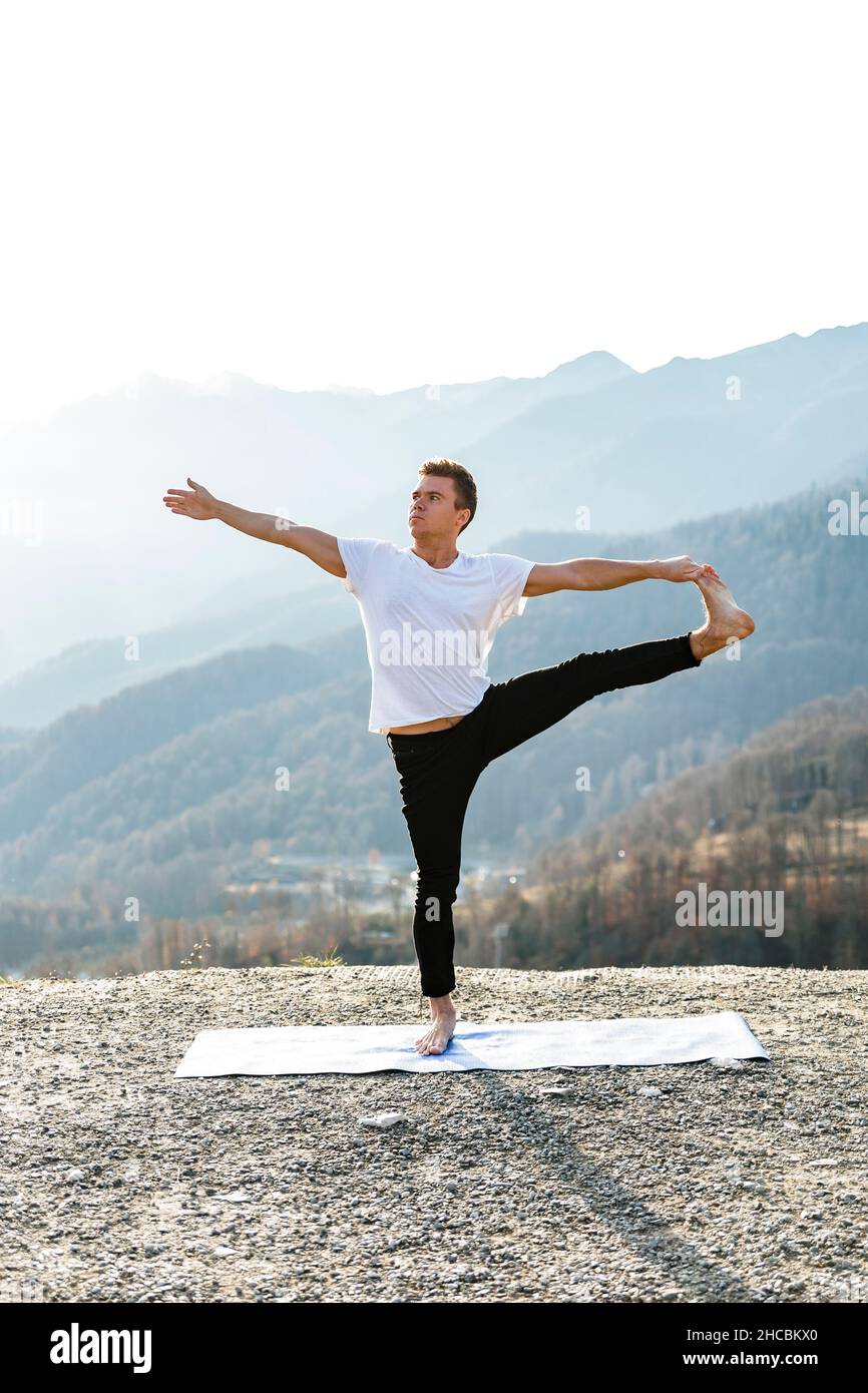 Mann balanciert sich auf einem Bein und übt Utthita Hasta Padangusthasana mit Bergblick Stockfoto