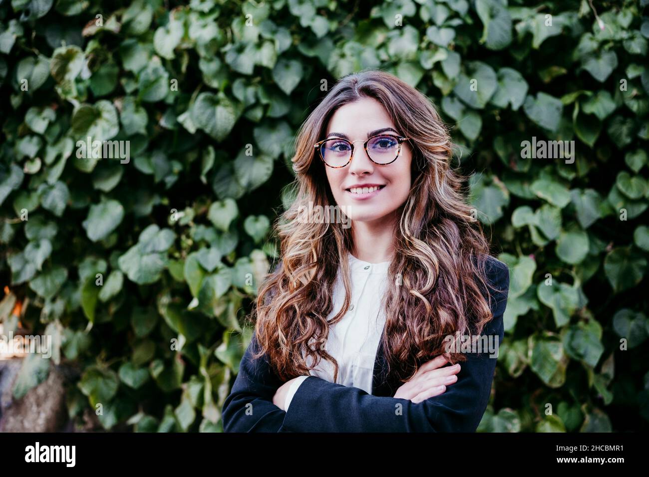 Junge Geschäftsfrau mit gekreuzten Armen vor der Hecke Stockfoto