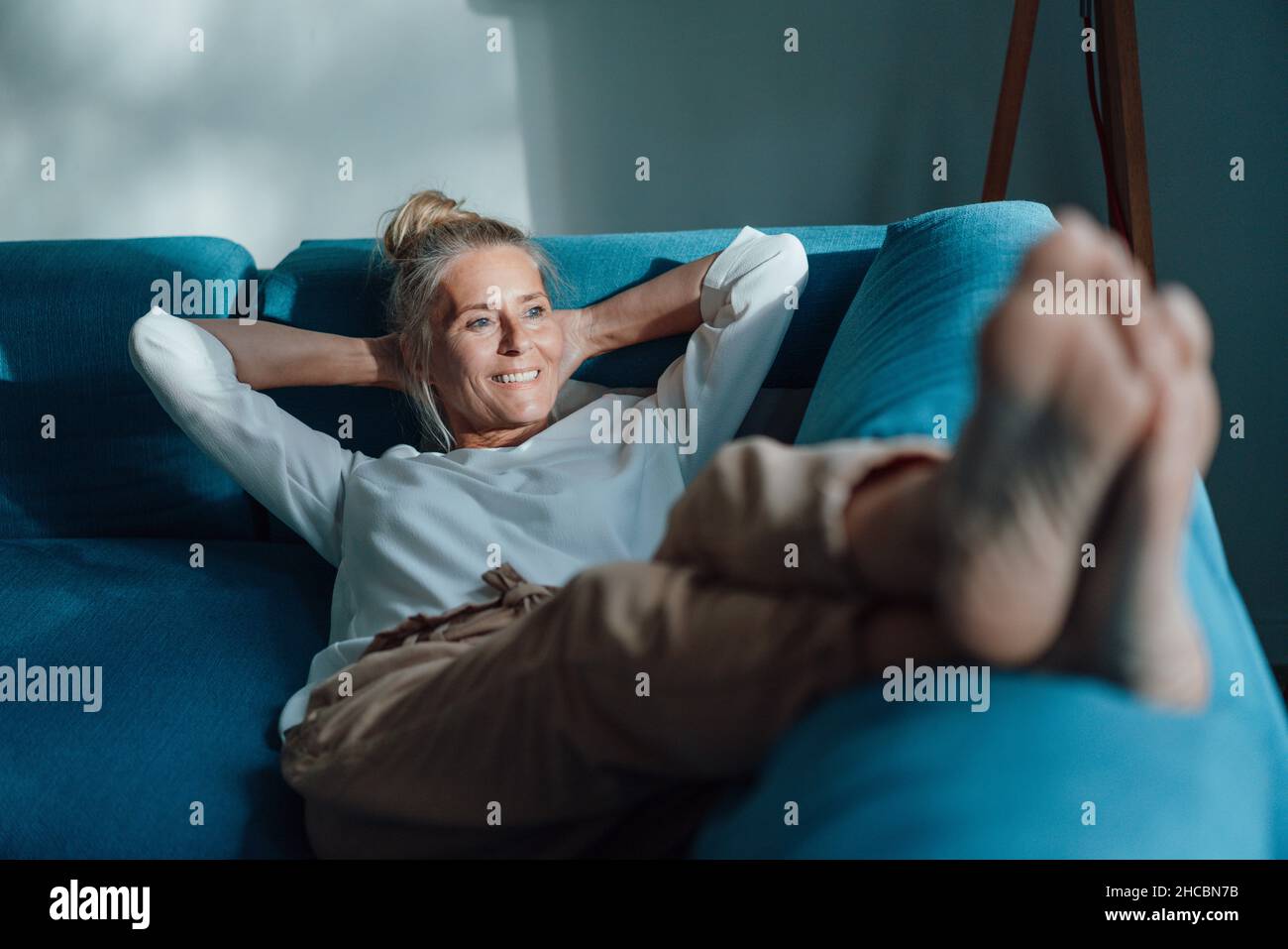 Lächelnde Frau mit Händen hinter dem Kopf auf dem Sofa Stockfoto