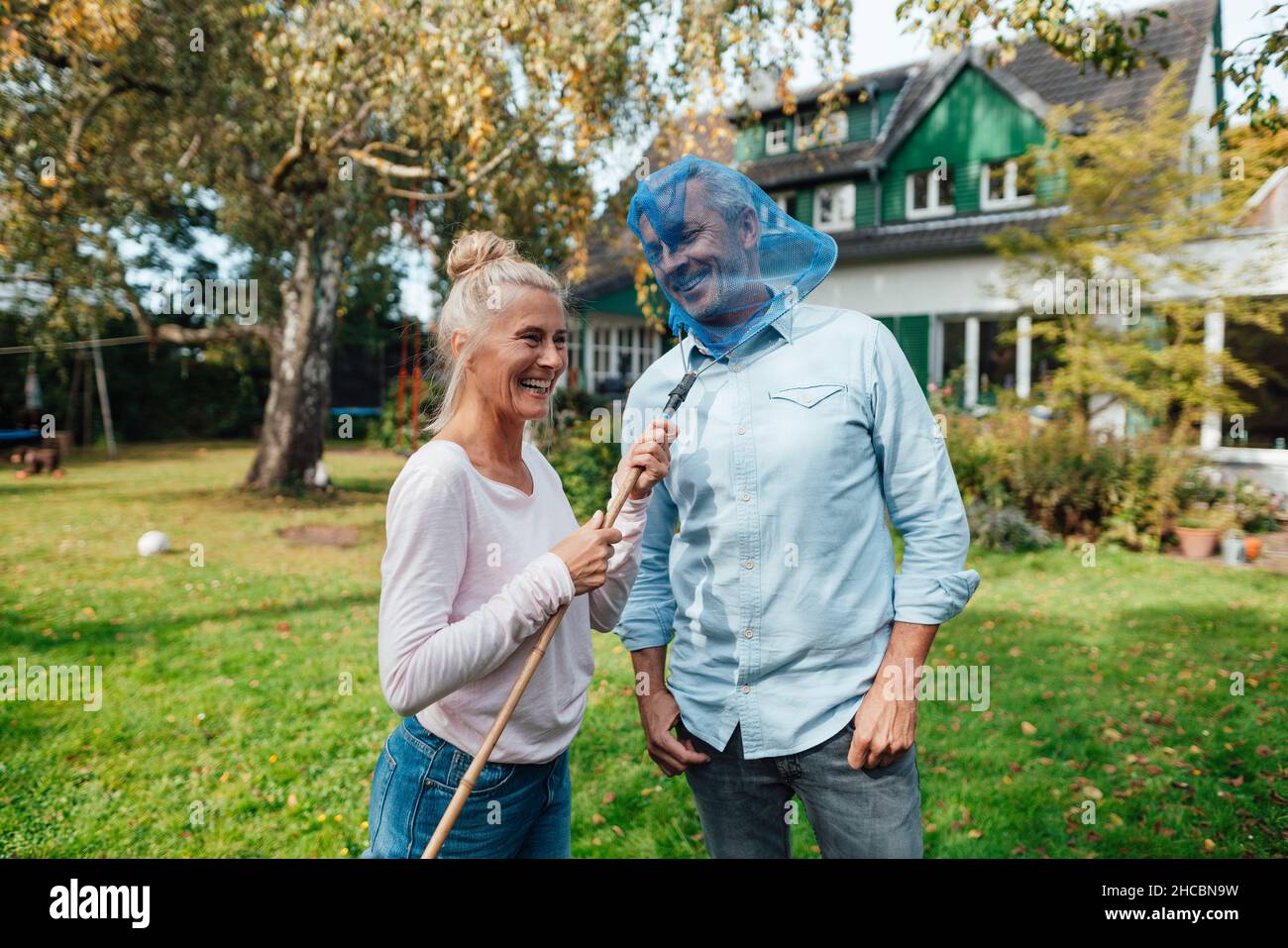 Verspielte Frau, die Schmetterlingsfischernetz auf das Gesicht des Mannes im Hinterhof setzt Stockfoto