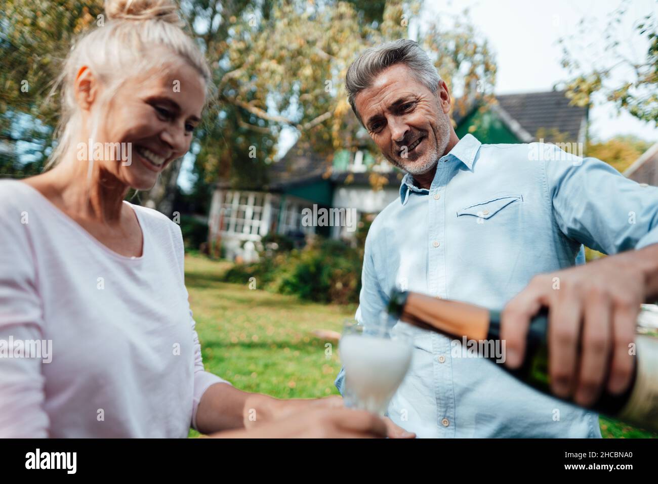 Lächelndes Paar mit einer Flasche Champagner und Flöte im Hinterhof Stockfoto