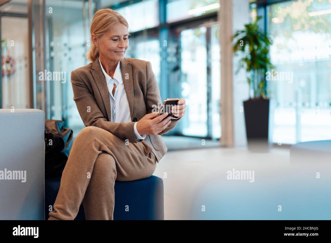 Nachdenkliche Geschäftsfrau, die im Büro mit gekreuzten Beinen am Knie sitzt Stockfoto