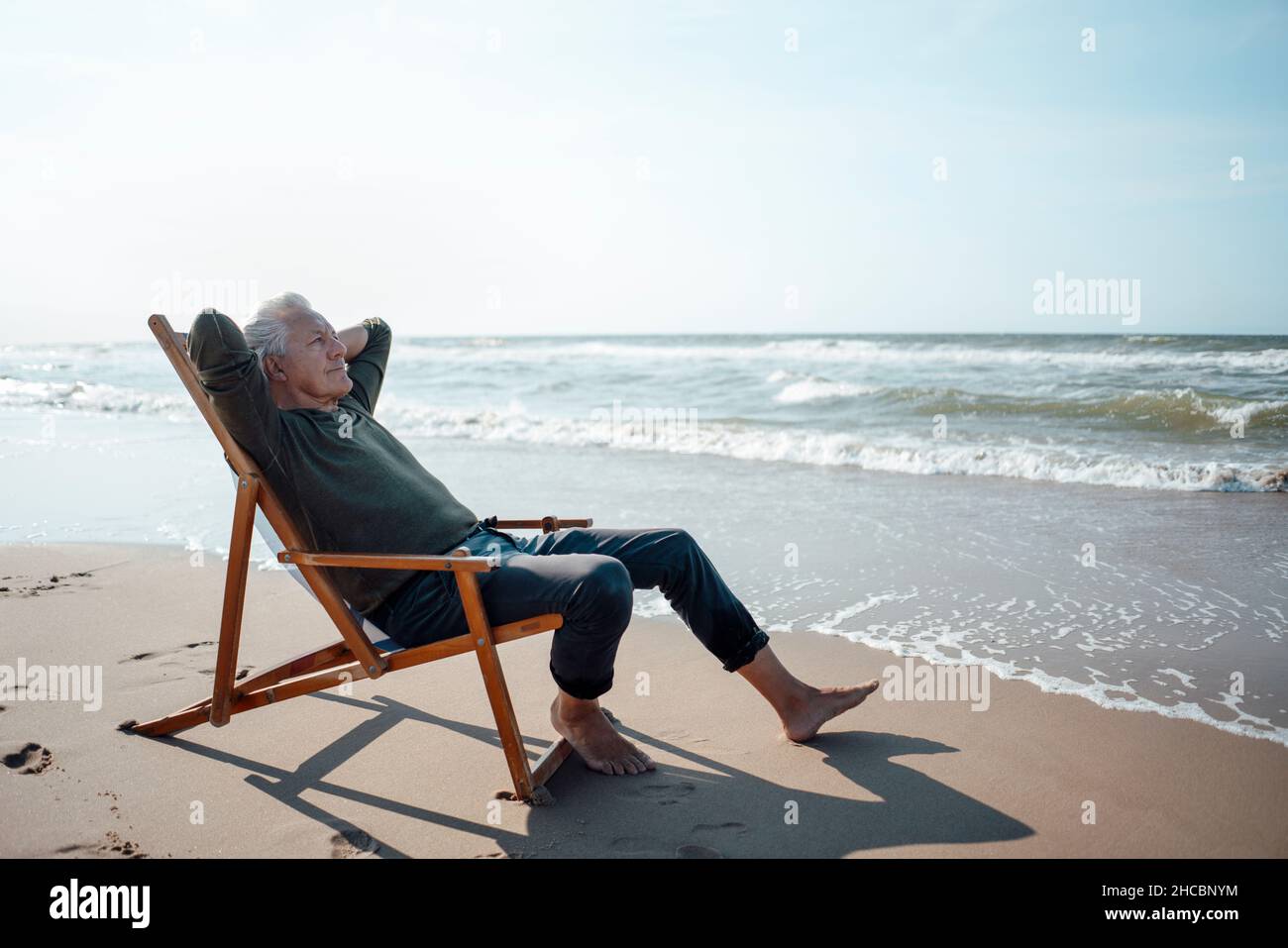 Älterer Mann, der das Meer beim Strandspaziergängen ansah Stockfoto