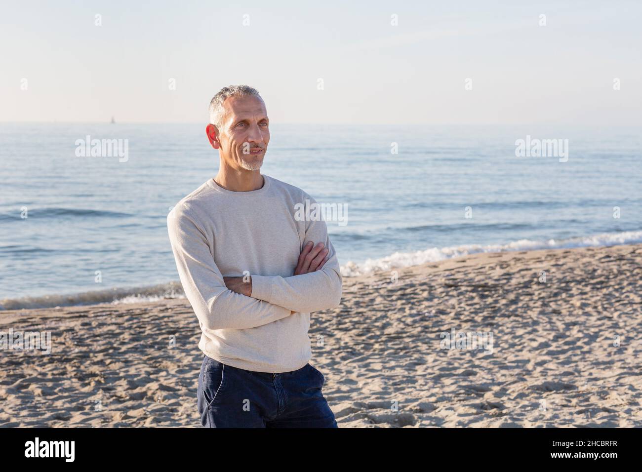 Mann, der mit gekreuzten Armen am Strand steht Stockfoto