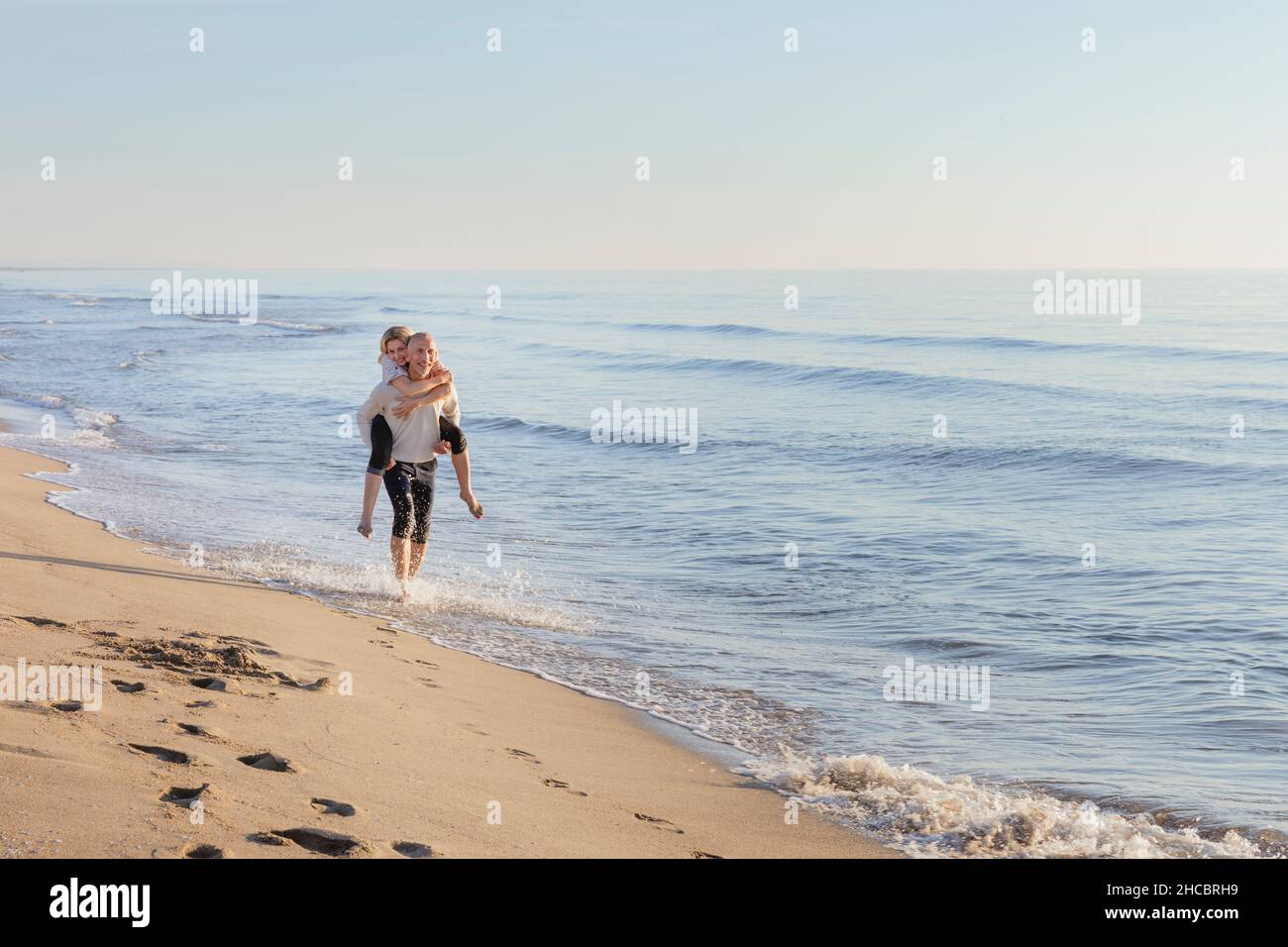 Mann, der der Frau am Strand eine Rutschfahrt gab Stockfoto