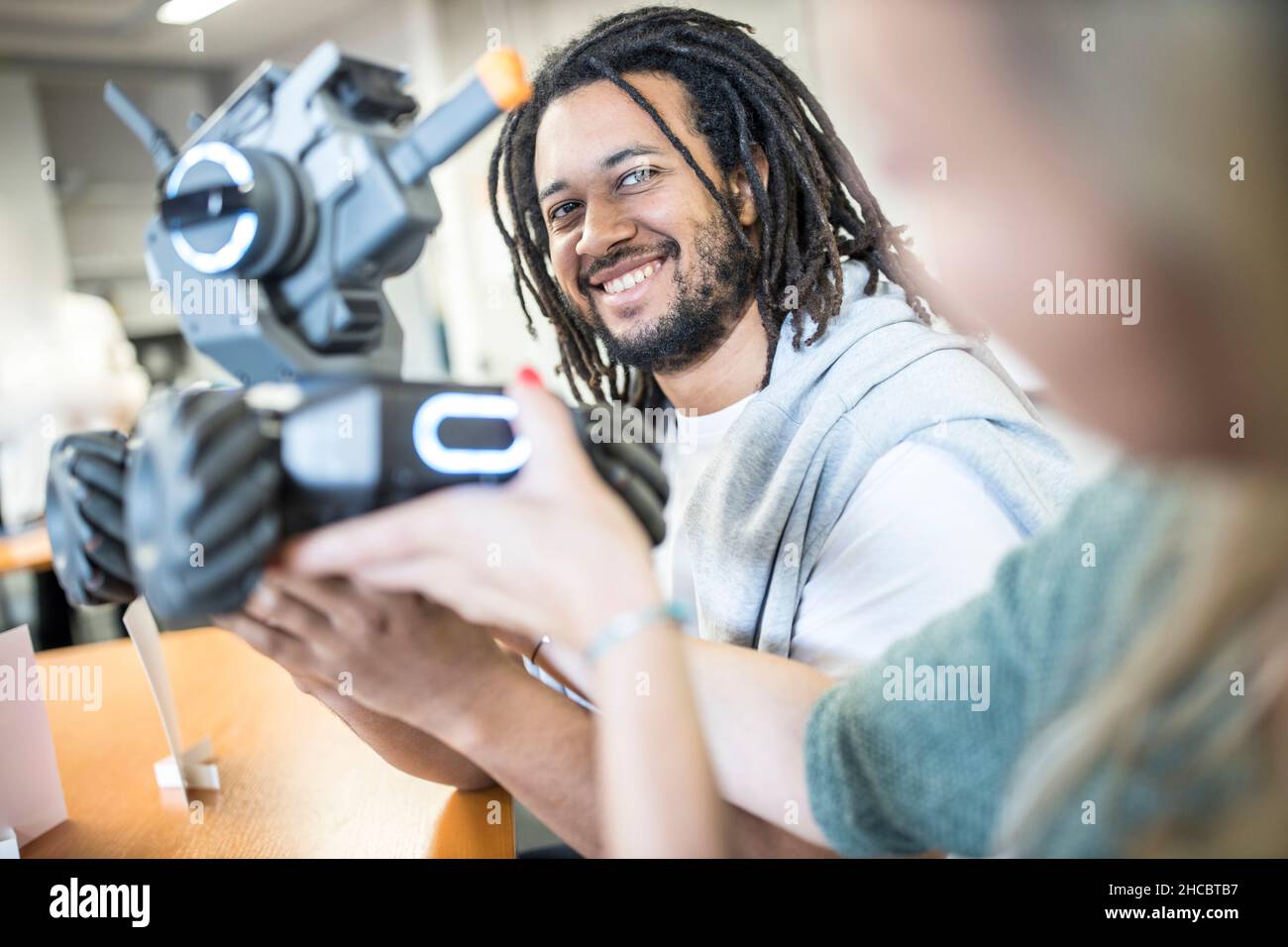 Junger Techniker schaut auf einen Ingenieur, der ein Roboterauto in der Werkstatt hält Stockfoto