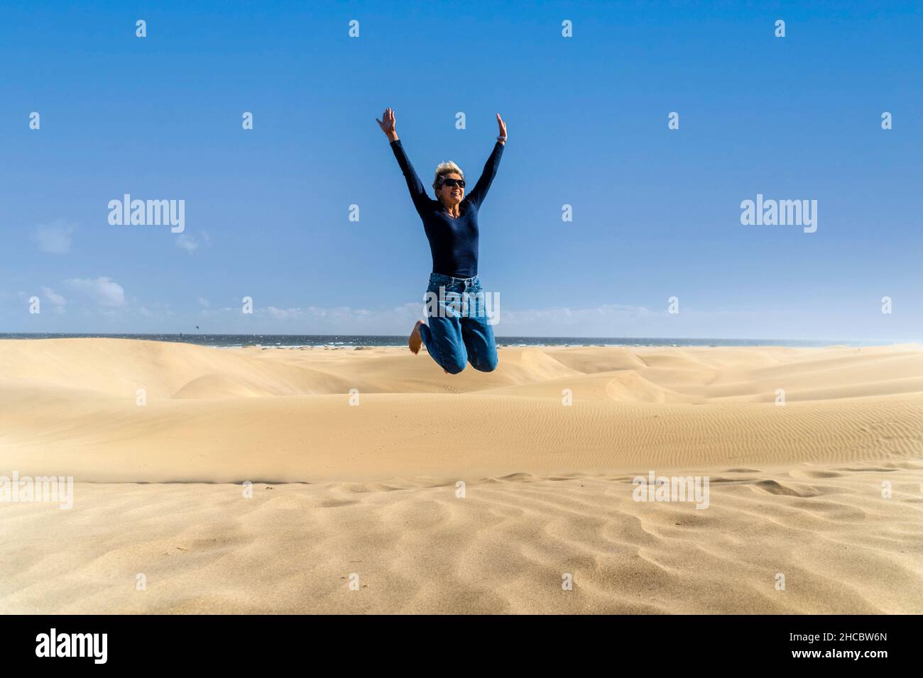 Glückliche Frau springt auf die Dünen im Maspalomas Nature Reserve, Gran Canaria, Kanarische Inseln, Spanien Stockfoto