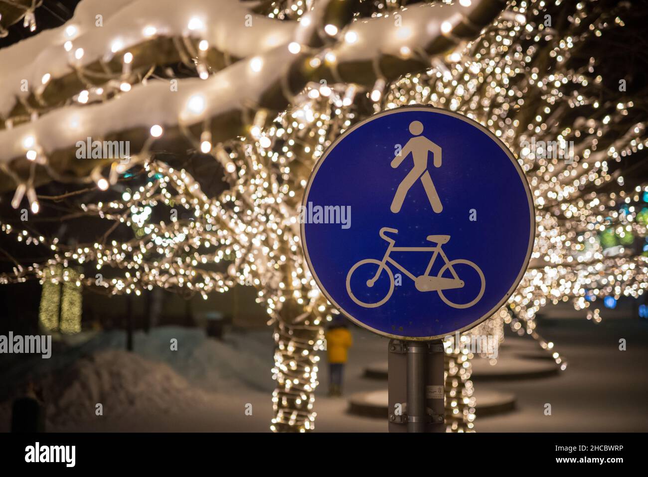Das Zeichen eines Radweges und ein Fußgänger auf der Straße im Winter mit schönen weihnachtslicht Bokeh im Park. Stockfoto