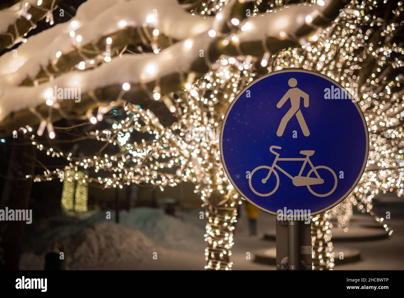 Das Zeichen eines Radweges und ein Fußgänger auf der Straße im Winter mit schönen weihnachtslicht Bokeh im Park. Stockfoto