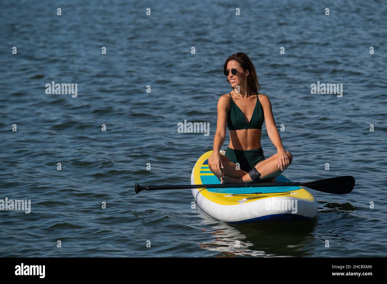 Kaukasische Frau sitzt in Lotusposition auf dem SUP-Brett auf dem See. Sommersport. Stockfoto