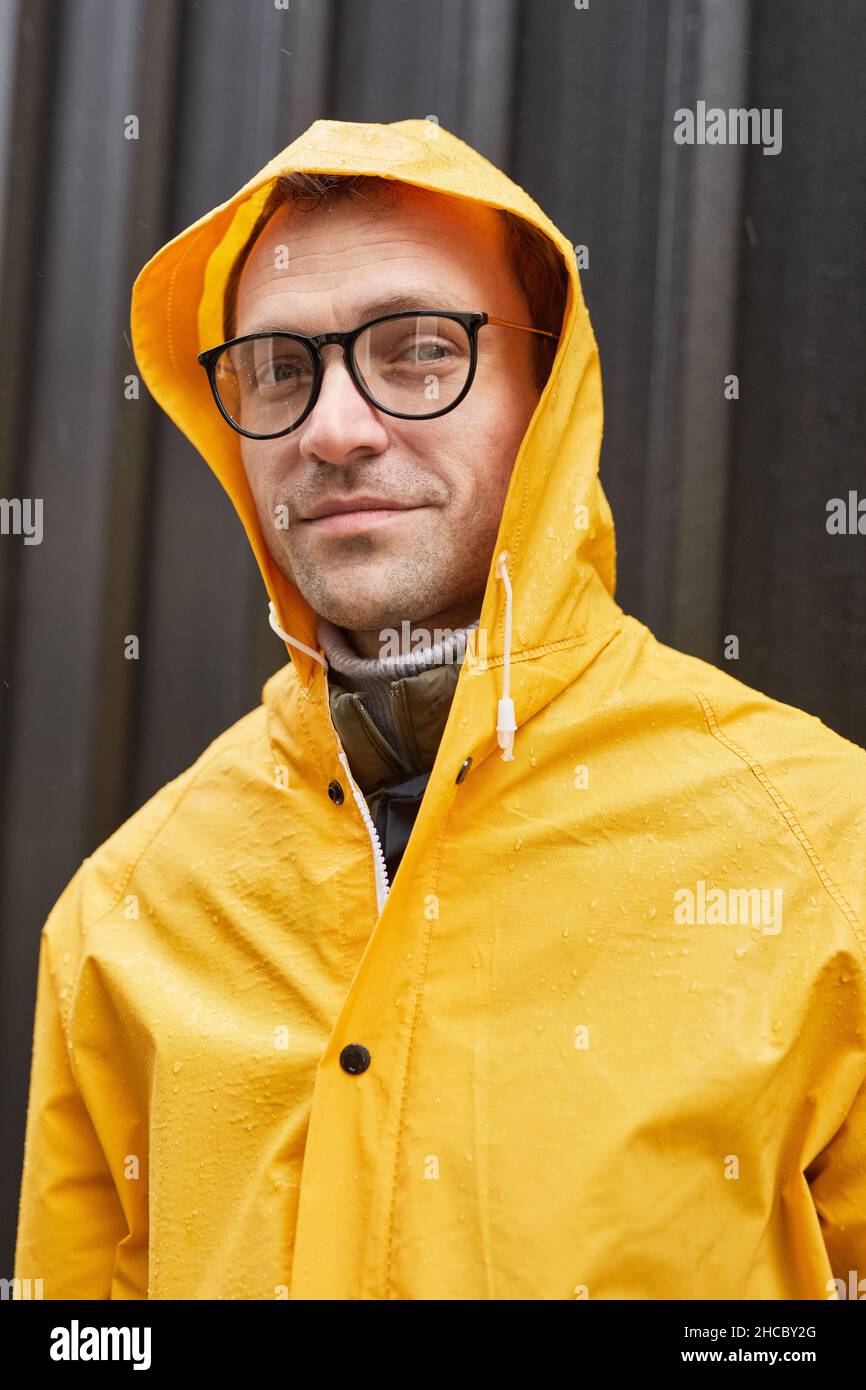 Vertikale, mittlere Nahaufnahme eines reifen Mannes mit gelber Regenjacke, der an regnerischen Tagen im Freien steht und die Kamera anschaut Stockfoto