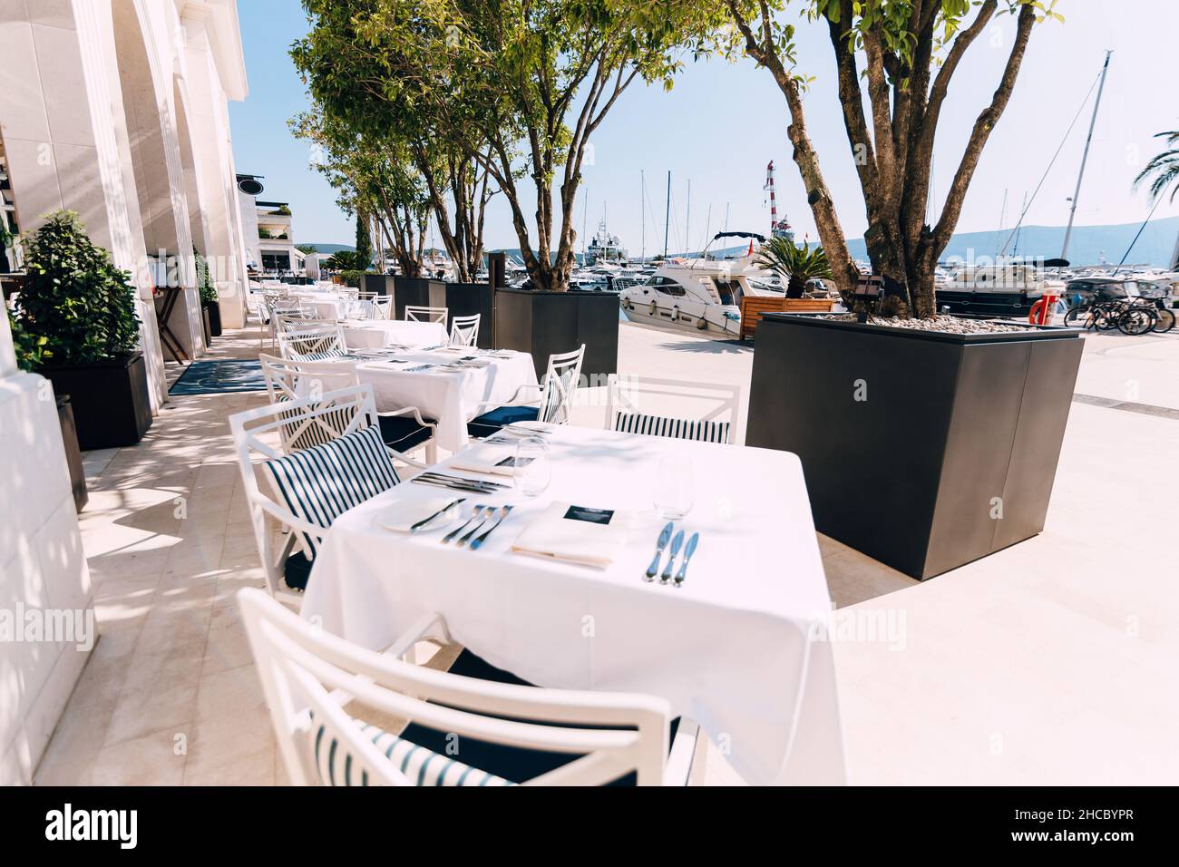 Tische mit weißen Tischdecken und Stühle am Meer neben dem Yachthafen mit festgedeckten Yachten Stockfoto