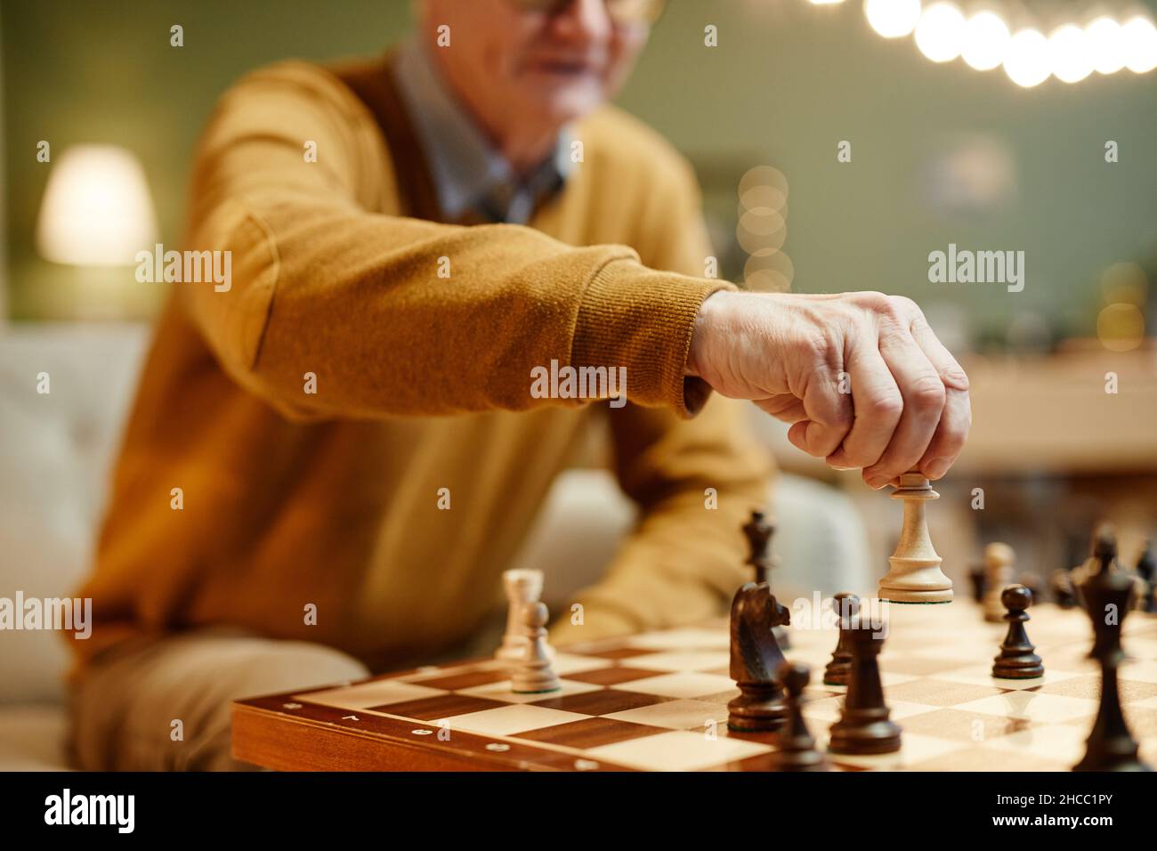 Unkenntlich kaukasischer Mann, der vor einem hölzernen Schachbrett mit Schachfigur in der Hand sitzt Stockfoto
