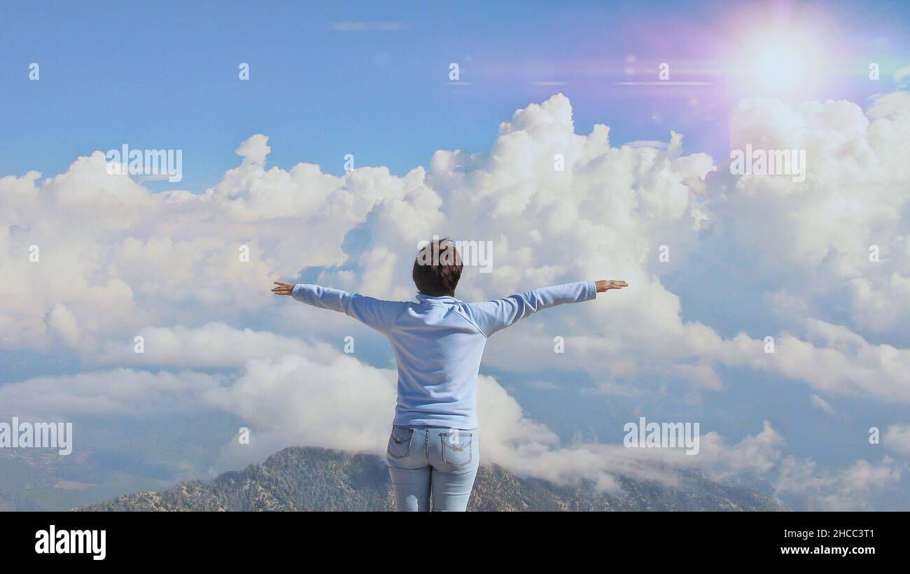 Die Frau steht an einem sonnigen Tag auf einem Berg in der Nähe des Abgrunds auf einem Hintergrund aus blauem Himmel und weißen Wolken Stockfoto