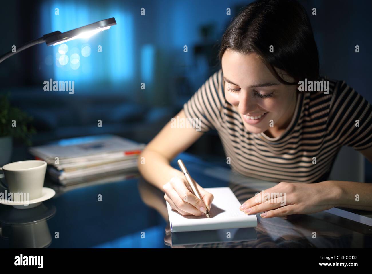 Glückliche Frau, die sich nachts zu Hause Notizen auf einem Notizbuch auf Papier macht Stockfoto