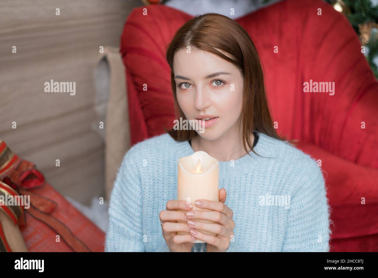 Neujahrs-Porträt einer schönen kaukasischen jungen Frau in hellblauem Pullover mit Kerze in den Händen. Weihnachtsferien. Hochwertige Fotos Stockfoto