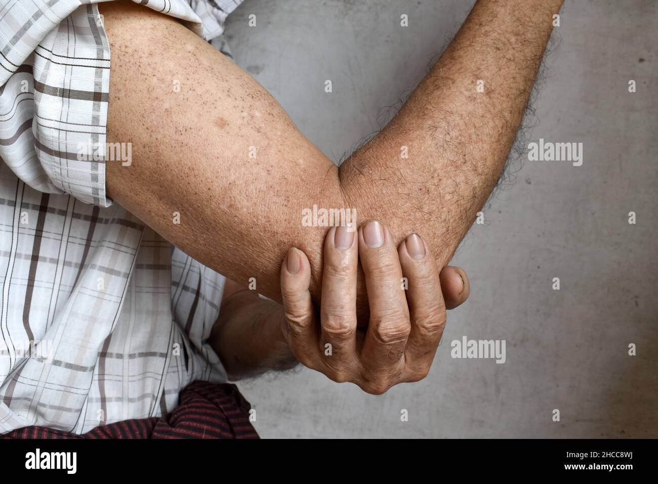 Schmerzen im Ellenbogengelenk des südostasiatischen älteren Mannes. Konzept von Ellenbogenschmerzen, rheumatoider Arthritis und Armproblemen. Stockfoto