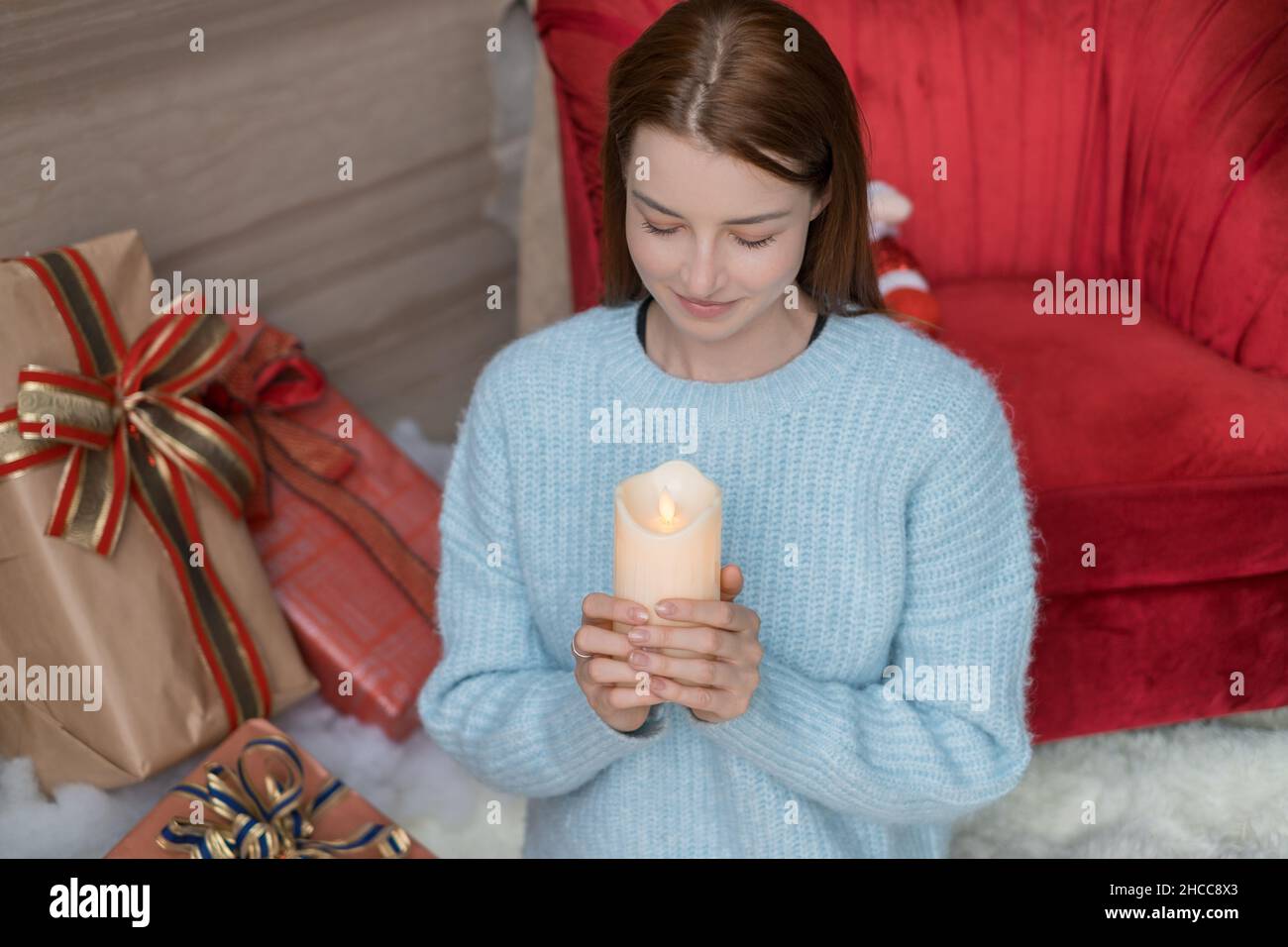 Neujahrs-Porträt einer schönen kaukasischen jungen Frau in hellblauem Pullover mit Kerze in den Händen. Weihnachtsferien. Hochwertige Fotos Stockfoto