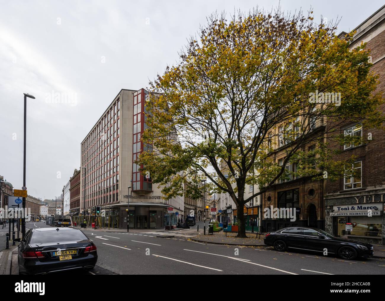 Vor den Geschäften und Büros in der Baldwin Street im Stadtzentrum von Bristol zeigt ein Straßenbaum Herbstfarben. Stockfoto