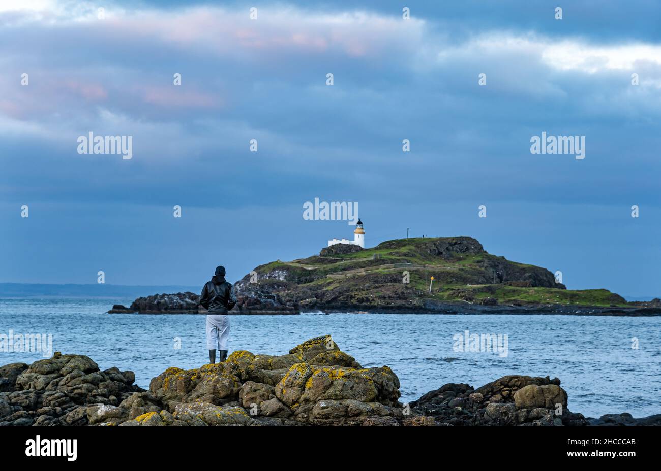 Junger Mann, der in der Dämmerung auf Felsen steht und auf Fidra Island, Firth of Forth, Schottland, Großbritannien, blickt Stockfoto