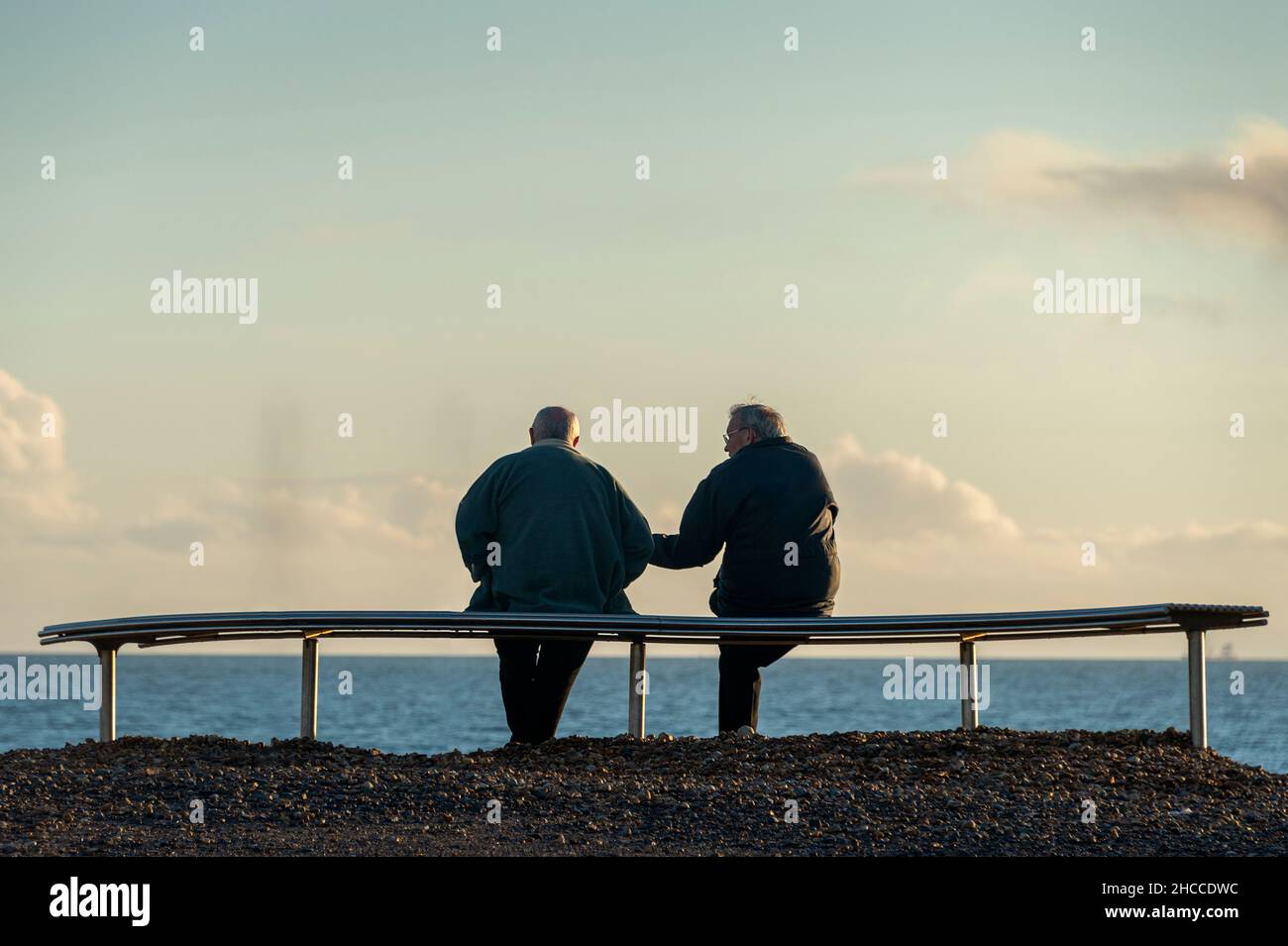 Rückansicht von zwei älteren Männern, die auf einer Bank am Meer sitzen und miteinander reden. Stockfoto